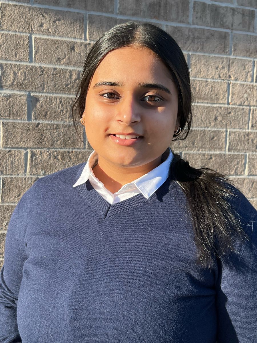 Prabhleen smiling, standing in front of a brick wall